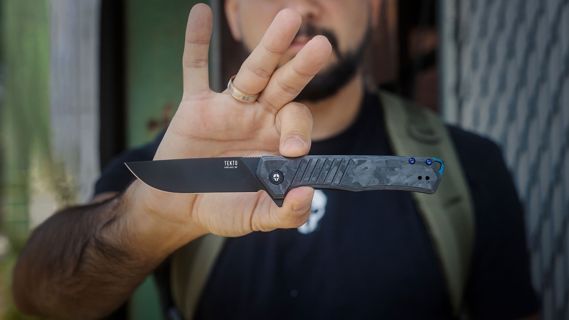 Man holding in hand Folding Knife F1 Alpha from Tekto Knives, with black titanium-coated blade and forged carbon handle.