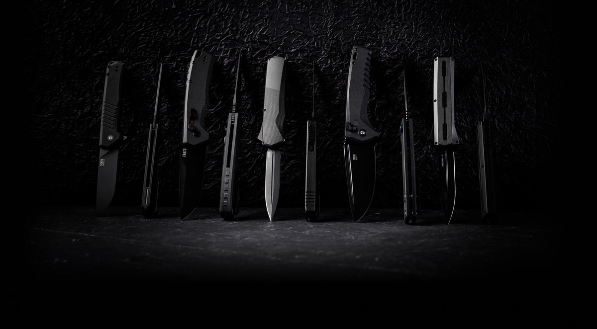 A lineup of TEKTO OTF, automatic and folding knives standing side by side on a dark textured surface